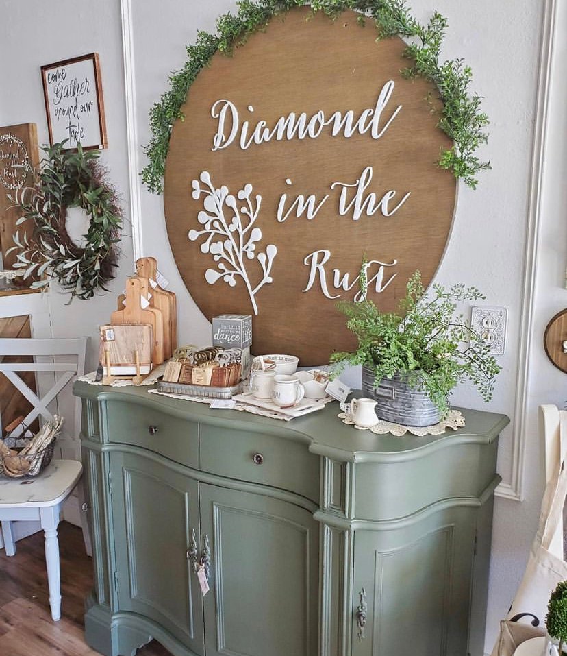 Diamond in the Rust round wooden sign above a sage green cabinet styled with cutting boards, mugs, and greenery