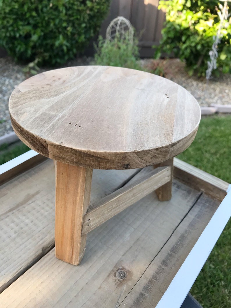 Round three-legged wood stool plant stand with a weathered rustic finish