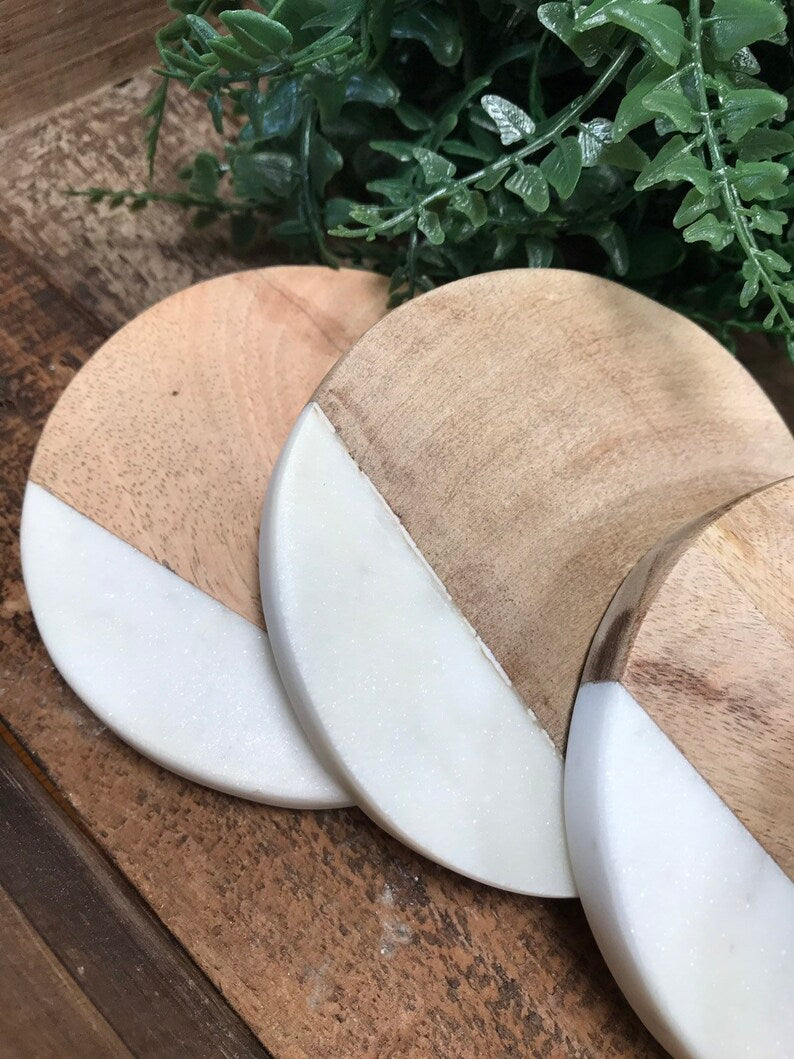 Four round coasters, each half light mango wood and half white marble, laid out on a wooden surface